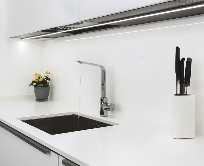Modern designer chrome water tap over stainless steel kitchen sink. Interior of bright white kitchen